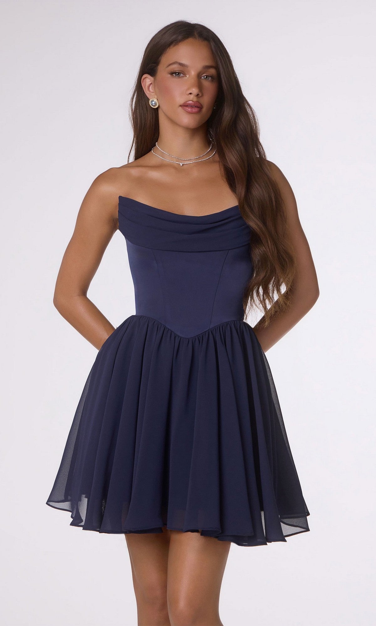 A woman wears the Amoris T740 short homecoming dress, featuring a strapless navy satin bodice and flared chiffon skirt, standing against a plain light background.